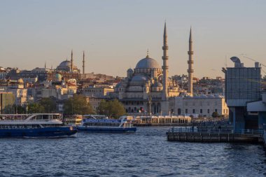 İstanbul 'daki Yeni Cami camii üzerinde günbatımında, Boğaz boyunca geleneksel feribotlar dolaşıyor. Osmanlı mimarisi ve Türk kültür başkentinin kentsel manzarası. İstanbul 20 Mayıs 2025