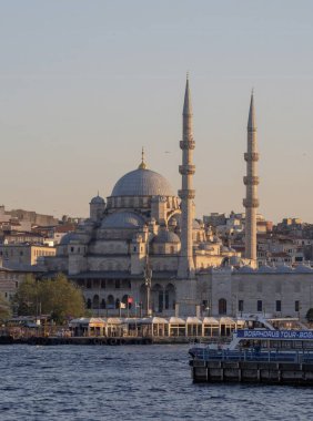 İstanbul 'daki Yeni Cami camii üzerinde günbatımında, Boğaz boyunca geleneksel feribotlar dolaşıyor. Osmanlı mimarisi ve Türk kültür başkentinin kentsel manzarası. İstanbul 20 Mayıs 2025