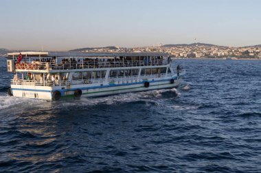 İstanbul, Türkiye 'deki İstanbul Boğazı' nda seyahat eden yolcu feribotları. Gemide bayraklı ve yolcuları olan deniz gemileri, şehrin silueti ve arka planda açık mavi su. 19 Mayıs 2025