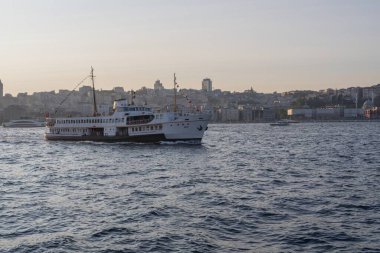 İstanbul, Türkiye 'deki İstanbul Boğazı' nda seyahat eden yolcu feribotları. Gemide bayraklı ve yolcuları olan deniz gemileri, şehrin silueti ve arka planda açık mavi su. 19 Mayıs 2025