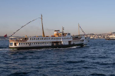 İstanbul, Türkiye 'deki İstanbul Boğazı' nda seyahat eden yolcu feribotları. Gemide bayraklı ve yolcuları olan deniz gemileri, şehrin silueti ve arka planda açık mavi su. 19 Mayıs 2025