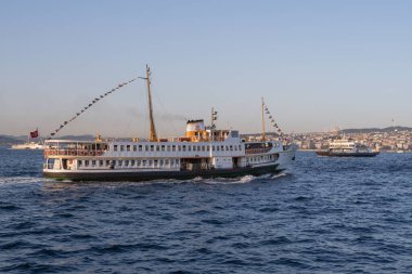 İstanbul, Türkiye 'deki İstanbul Boğazı' nda seyahat eden yolcu feribotları. Gemide bayraklı ve yolcuları olan deniz gemileri, şehrin silueti ve arka planda açık mavi su. 19 Mayıs 2025
