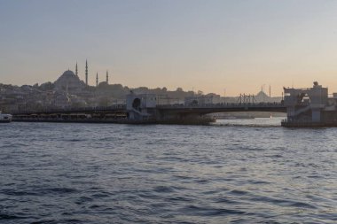 İstanbul semalarında gün batımı, Süleyman Camii, Boğaz ve liman boyundaki teknelerle birlikte yükseliyor. Türk ikonik şehri üzerinde tarihi Osmanlı mimarisi ve sakin akşam atmosferi.