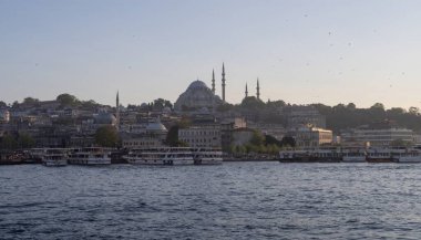 İstanbul semalarında gün batımı, Süleyman Camii, Boğaz ve liman boyundaki teknelerle birlikte yükseliyor. Türk ikonik şehri üzerinde tarihi Osmanlı mimarisi ve sakin akşam atmosferi.