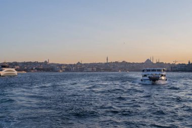İstanbul, Türkiye 'deki İstanbul Boğazı' nda seyahat eden yolcu feribotları. Gemide bayraklı ve yolcuları olan deniz gemileri, şehrin silueti ve arka planda açık mavi su. 19 Mayıs 2025