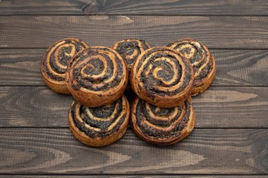 Ahşap masada lezzetli haşhaş tohumu ruloları. Haşhaş tohumlarıyla dolu, sarmal dizaynlı ve çıtır çıtır çıtır taze hamur işleri. Geleneksel ev yapımı tatlı, yeşil bitki yapraklarıyla servis edilir..