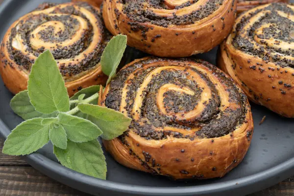 Lezzetli haşhaşlı hamur tatlısı, kırsal ahşap arka planda siyah tabakta dönüyor. Geleneksel fırında pişirilmiş, sarmal dokulu tatlıya yakın çekim. Fırın, ev yapımı tatlılar, tatlı yiyecekler ve atıştırmalıklar için ideal.