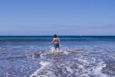 Tenerife, Kanarya Adaları 'nda yaz sahnesi. İnsanlar yüzüyor, volkanik kumda dinleniyor, dalgalar sıçrıyor, ve volkanik kayalar yosunlarla kaplı manzaralı dağ manzarası ve okyanus manzarası.