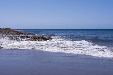  Kumlu sahilde volkanik kayalara vuran okyanus dalgaları. Doğal dokuları ve açık ufku olan kıyı deniz manzarası. Tenerife, Kanarya Adaları, İspanya.