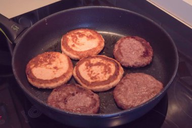 Fried chicken cutlets and beef patties cooking in pan on stovetop. Golden crust, homemade meal preparation, protein food background, culinary process of frying meat cutlets and burgers.