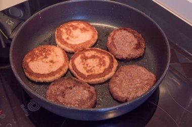 Fried chicken cutlets and beef patties cooking in pan on stovetop. Golden crust, homemade meal preparation, protein food background, culinary process of frying meat cutlets and burgers.