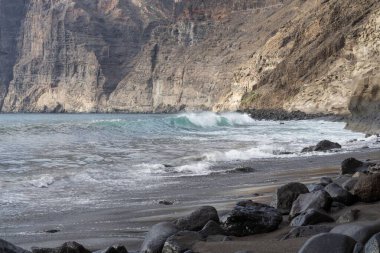 İspanya 'nın Tenerife adasındaki kayalara ve sarp kayalıklara vuran siyah volkanik plajlar. Güçlü deniz sörfü, engebeli kıyı şeridi ve yumuşak gün ışığında Atlantik kıyısının jeolojik oluşumları..