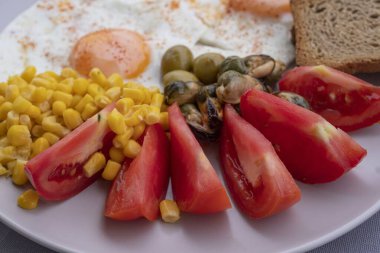 Yumurta, mısır, zeytin, midye ve tabakta tam tahıllı tost ile servis edilen taze domatesli sağlıklı bir kahvaltı. Besleyici protein öğünleri, dengeli diyet yemekleri, Akdeniz kahvaltısı..