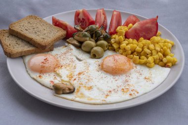 Yumurta, mısır, zeytin, midye ve tabakta tam tahıllı tost ile servis edilen taze domatesli sağlıklı bir kahvaltı. Besleyici protein öğünleri, dengeli diyet yemekleri, Akdeniz kahvaltısı..