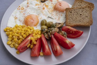Yumurta, mısır, zeytin, midye ve tabakta tam tahıllı tost ile servis edilen taze domatesli sağlıklı bir kahvaltı. Besleyici protein öğünleri, dengeli diyet yemekleri, Akdeniz kahvaltısı..