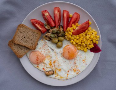 Yumurta, mısır, zeytin, midye ve tabakta tam tahıllı tost ile servis edilen taze domatesli sağlıklı bir kahvaltı. Besleyici protein öğünleri, dengeli diyet yemekleri, Akdeniz kahvaltısı..