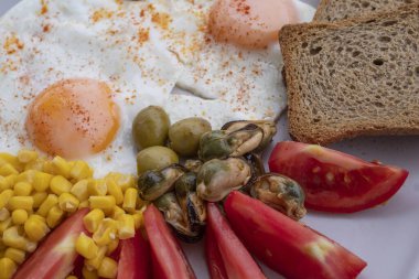 Yumurta, mısır, zeytin, midye ve tabakta tam tahıllı tost ile servis edilen taze domatesli sağlıklı bir kahvaltı. Besleyici protein öğünleri, dengeli diyet yemekleri, Akdeniz kahvaltısı..