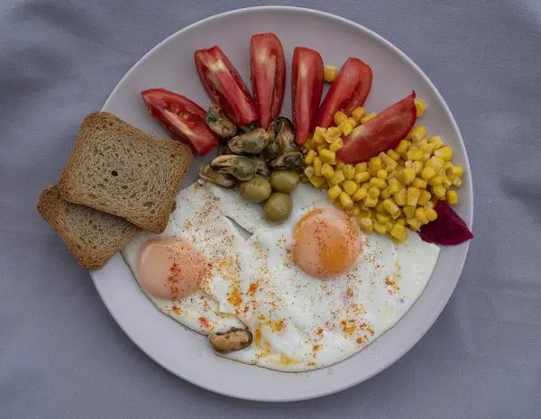Yumurta, mısır, zeytin, midye ve tabakta tam tahıllı tost ile servis edilen taze domatesli sağlıklı bir kahvaltı. Besleyici protein öğünleri, dengeli diyet yemekleri, Akdeniz kahvaltısı..