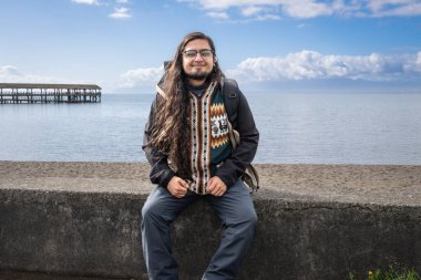 Puerto Varas, Los Lagos, Chile. Young man traveler - tourist next to the snow-capped volcano Osorno and Lake Llanquihue as seen from the city of Puerto Varas in Chilean Patagonia clipart