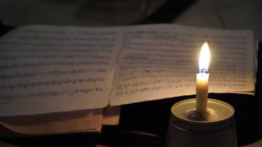 A burning candle on a metal surface illuminates an open sheet of music in a dimly lit environment, creating a nostalgic and intimate atmosphere. clipart