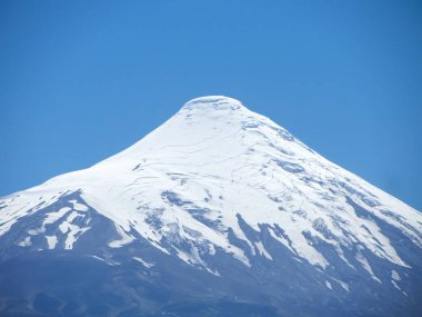 Osorno yanardağının görkemli manzarası, karla kaplı zirvesi ve engebeli yamaçları, Şili Patagonya 'da canlı mavi bir gökyüzüne karşı duruyor.