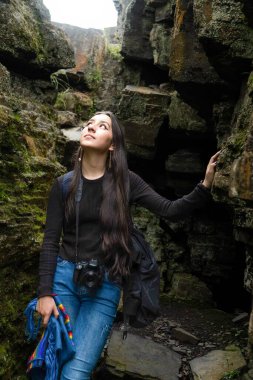 Kameralı maceraperest genç bir kadın yosun kaplı kayalık bir kanyonu keşfediyor, huşu içinde yukarı bakıyor. Doğal manzara ve açık hava fotoğrafçılığı