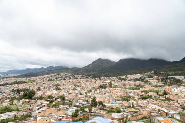 Bogota 'nın panoramik hava manzarası. Düşük katlı ve yüksek katlı binalar, yeşil alanlar ve bulutlu bir gökyüzünün altındaki uzak bir gökyüzü.