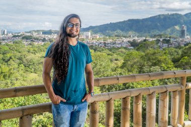 Bambu korkuluklarda neşeli bir adam yeşil manzaranın panoramik manzarasının ve arka planda gökyüzünün keyfini çıkarıyor.