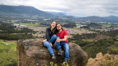  Gülümseyen bir çift, bir kayanın üzerinde otururken keyifli bir anın tadını çıkarıyor. Vadi, kasaba ve dağların panoramik manzarasıyla. Güzel bir açık hava macerası.