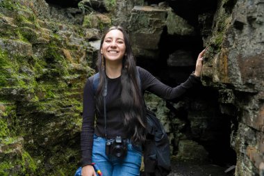 Kameralı maceraperest genç bir kadın yosun kaplı kayalık bir kanyonu keşfediyor, huşu içinde yukarı bakıyor. Doğal manzara ve açık hava fotoğrafçılığı