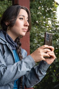 Frutillar, Şili 'deki Alman Koloni Müzesi' nde akıllı telefonuyla gülümseyen genç bir İspanyol kaşif. Bir Alman evinin yakınındaki turist fotoğraf çekiyor.