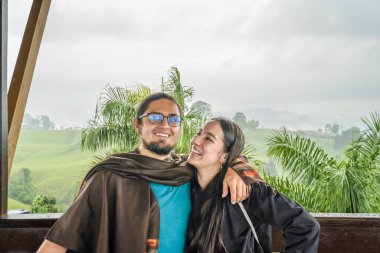 Genç Latin gezgin çift, arka planda şehir silüeti olan yeşil bir manzaranın panoramik manzarasının tadını çıkarıyor..