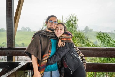 Genç Latin gezgin çift, arka planda şehir silüeti olan yeşil bir manzaranın panoramik manzarasının tadını çıkarıyor..