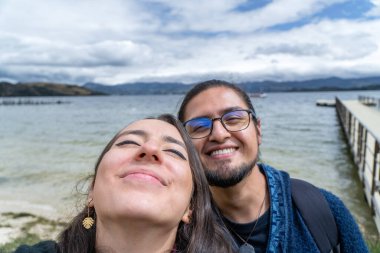 Yürüyüşe çıkmış gülümseyen genç bir çift. Gölde gülümseyen gezginler selfie çekiyorlar.