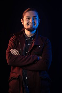 Sıcak bir gülümsemesi ve çapraz kolları olan kendine güvenen bir adam kasvetli mavi ve sıcak ışık altında karanlık bir arka plana karşı sanatsal ve şık bir portre yaratıyor..