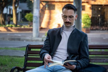 İspanyol bir adam parkta oturmuş kitap okuyor.