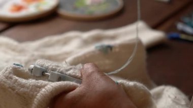 Bir insan, iğne ve mavi iplik kullanarak yumuşak, kabarık bir kumaşa dikkatlice bir tasarım işliyor..