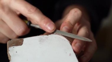 Bakır bir parçanın kenarını yumuşatmak için metal bir dosya kullanan bir zanaatkarın yakın çekimi. Çömlekçilik ve metal işlerinde ustalık..