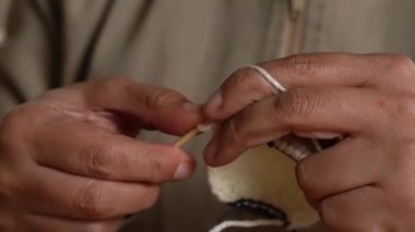 Beyaz yün iplik ve ahşap masada metal iğnelerle örgü ören ellerin yakın çekimi..