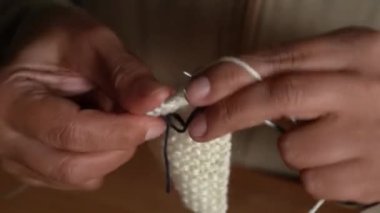 Beyaz yün iplik ve ahşap masada metal iğnelerle örgü ören ellerin yakın çekimi..