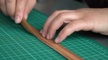 Zanaatkâr ellerin yakın plan çekimleri deri mücevher kutusunu yeşil hasırda hassas aletlerle şekillendiriyor..