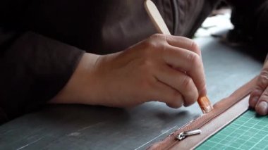 Zanaatkâr ellerin yakın plan çekimleri deri mücevher kutusunu yeşil hasırda hassas aletlerle şekillendiriyor..