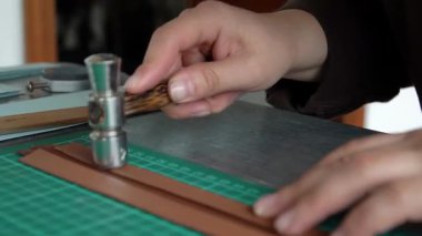 Zanaatkâr ellerin yakın plan çekimleri deri mücevher kutusunu yeşil hasırda hassas aletlerle şekillendiriyor..