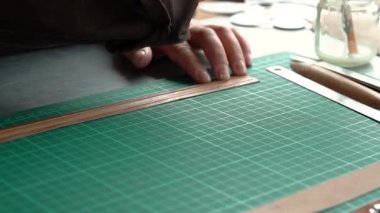 Zanaatkâr ellerin yakın plan çekimleri deri mücevher kutusunu yeşil hasırda hassas aletlerle şekillendiriyor..
