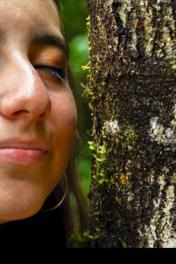 Genç bir kadın, yosun ve yosunla kaplı bir ağaç gövdesini yakından inceleyerek doğanın detaylarını takdir eder.