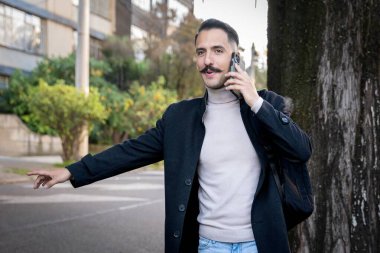 Sokakta iş adamı telefonda konuşurken taksi çeviriyor.