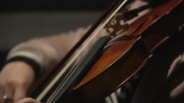 Kadın keman çalıyor, müzisyenin eli, yay ve enstrüman arasındaki hassas etkileşimi vurguluyor..