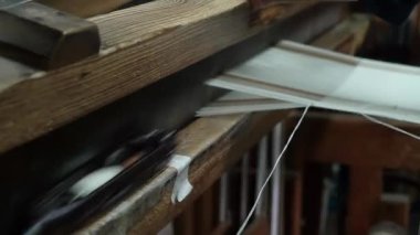 Geleneksel bir dokuma tezgahı işleten beyaz bir tekstil dokuyan bir elin yakın çekimi. Konferansta, dokuma tezgahının karmaşık süreci ve ahşap yapısı üzerinde duruluyor..