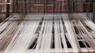 Dokuma tezgahına uzanan ipliklerin detaylı görüntüsü, dokuma işlemi için hazır. Odak noktası warp ipliklerinin paralel düzenlenmesi, dokuma tezgahının yapısı ve dokusu..