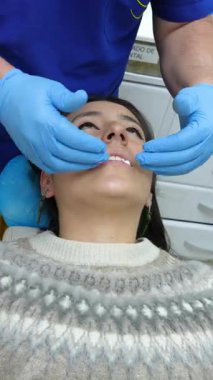 Mavi eldivenli bir dişçi sözlü muayene ya da prosedür için hazırlanırken bir kadın dişçi koltuğunda yatıyor..